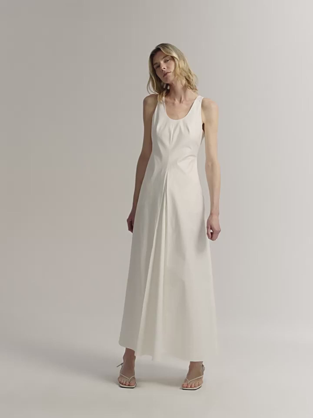 Woman wearing a white sleeveless dress against a plain background