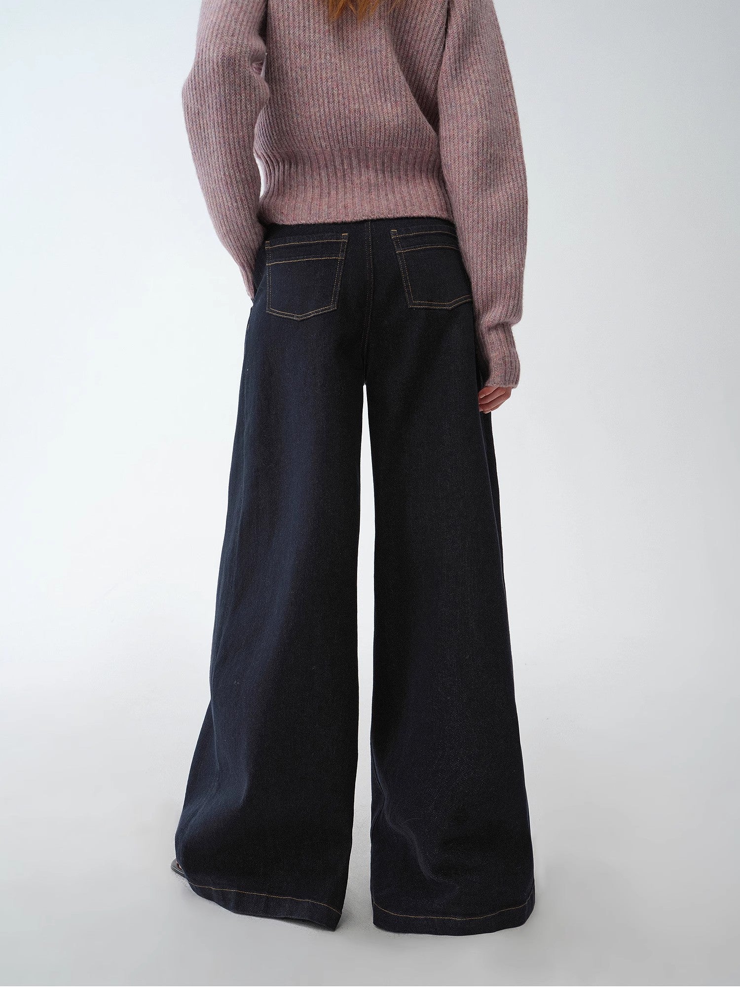 Person wearing a pink sweater and black wide-leg jeans on a white background