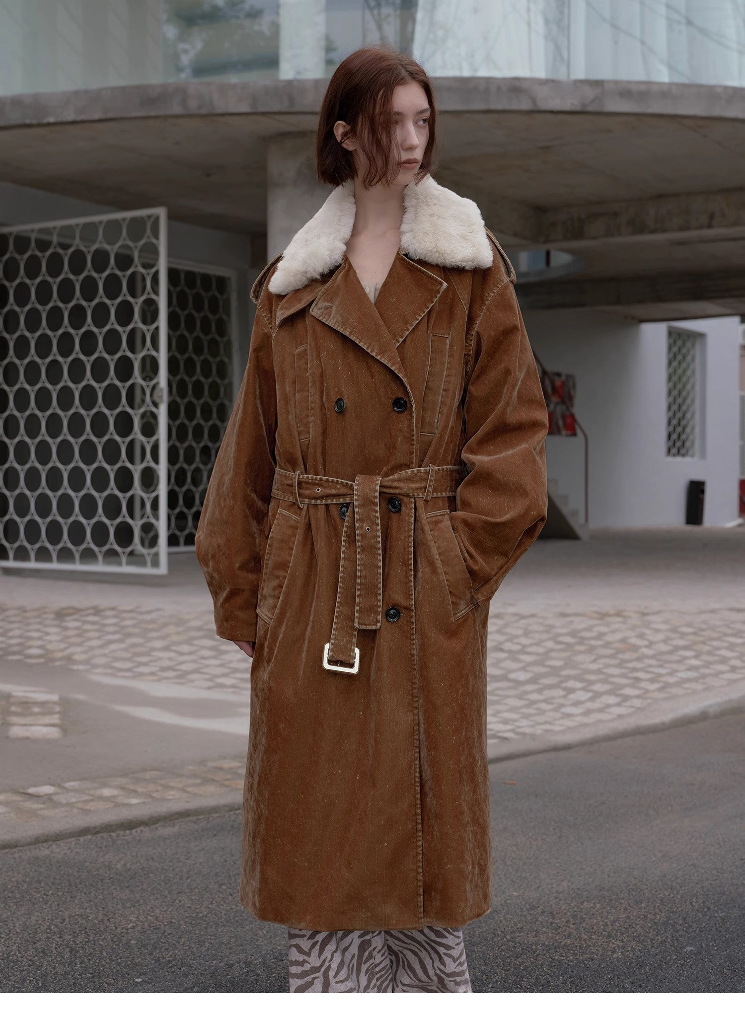 Person wearing a brown trench coat with white fur collar in an urban setting
