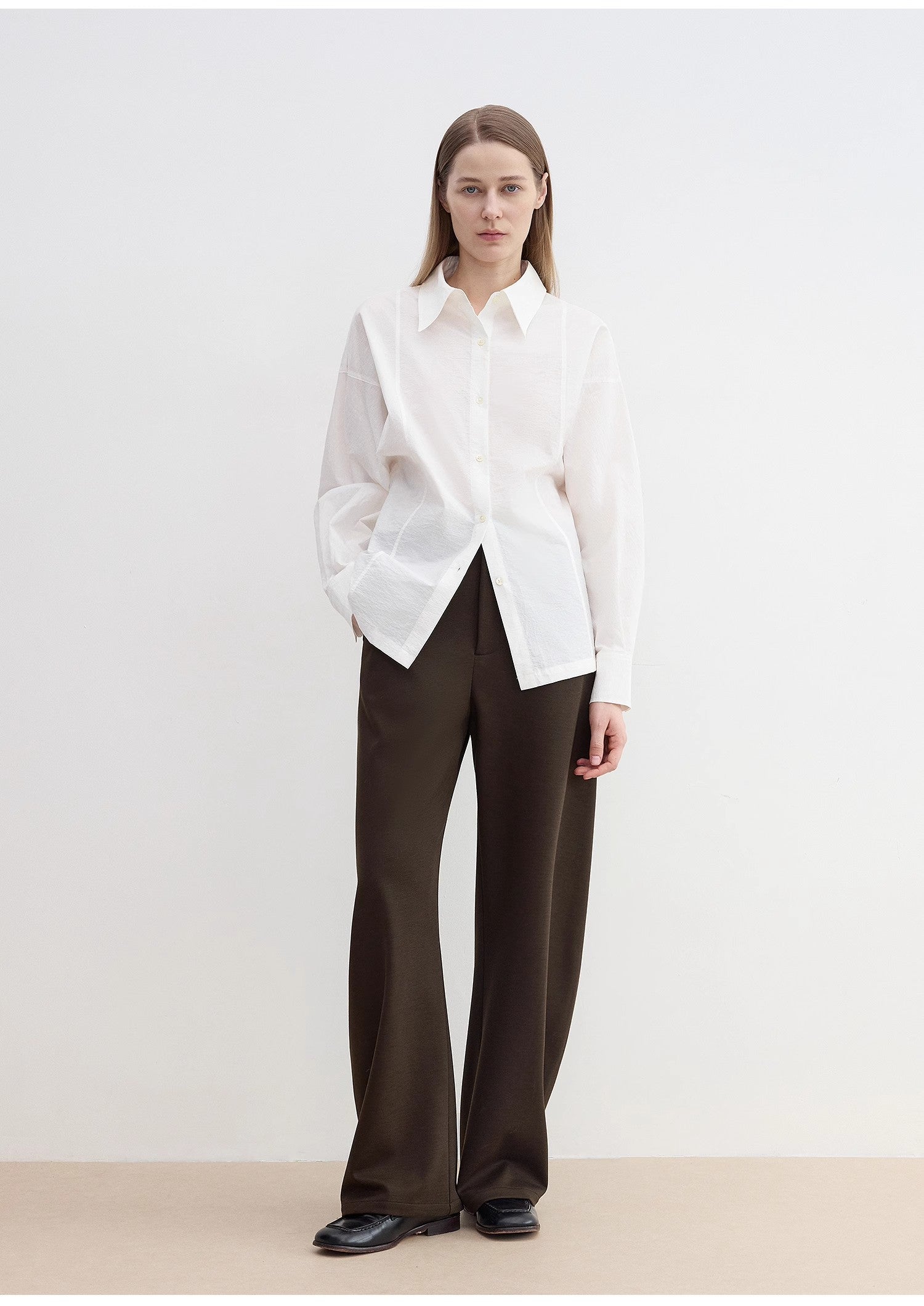Person wearing a white shirt and dark pants on a plain background