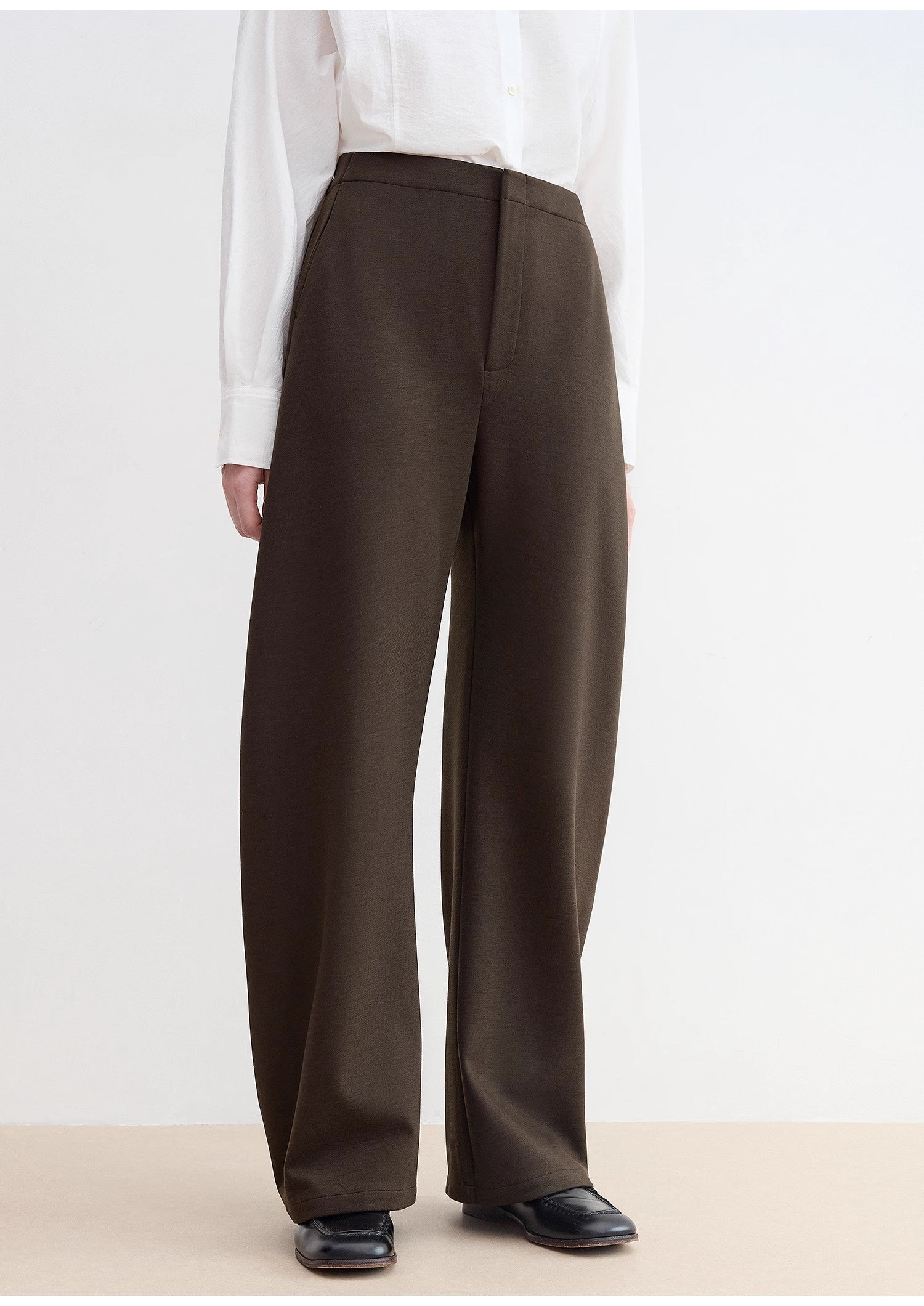 Brown wide-leg pants worn with a white shirt on a plain background