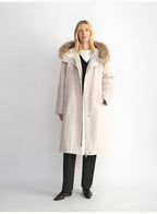 Woman wearing a long beige coat with fur hood on a white background