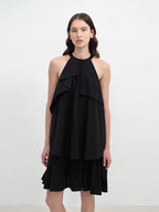 Woman wearing a black halter neck dress with ruffled layers on a white background