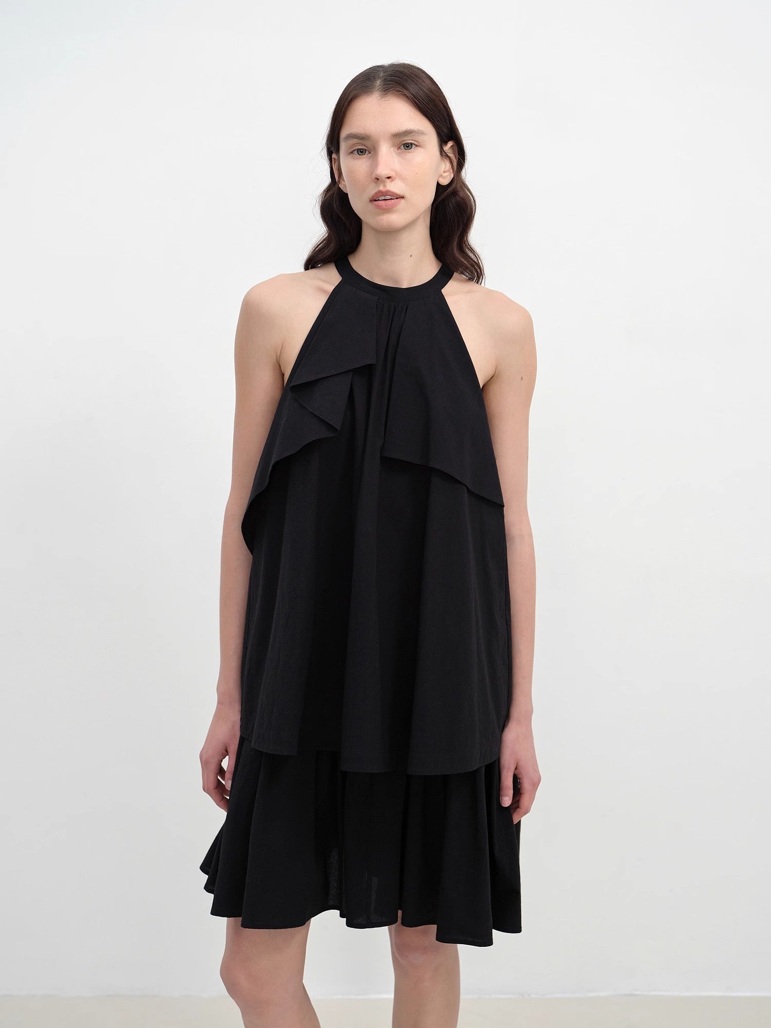 Woman wearing a black halter neck dress with ruffled layers on a white background
