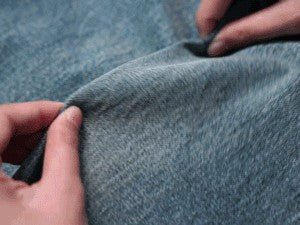 Close-up of blue denim fabric with hands manipulating it