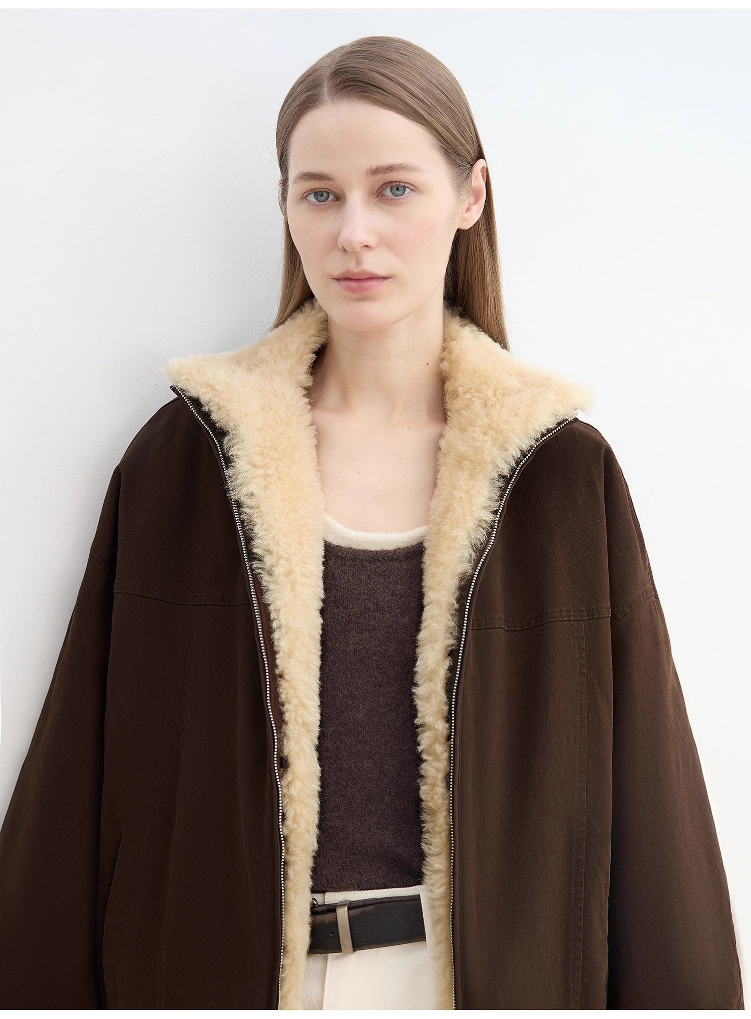 Woman wearing a brown coat with beige fur lining against a white background