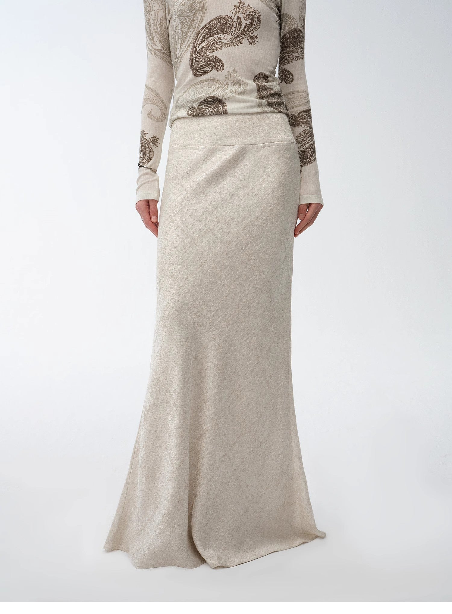 Person wearing a long beige skirt with a patterned top on a white background