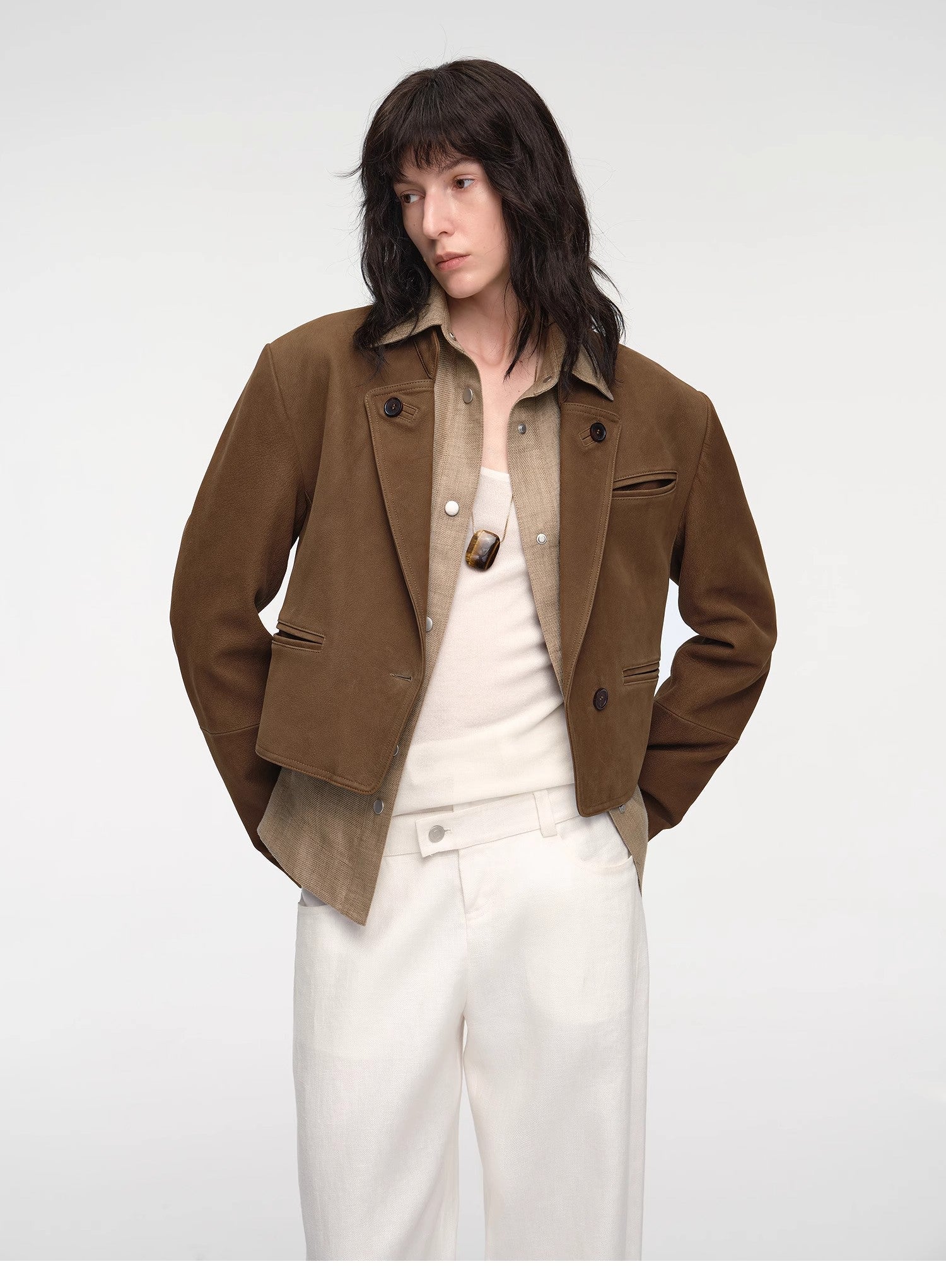 Person wearing a brown jacket over a white shirt and pants on a white background