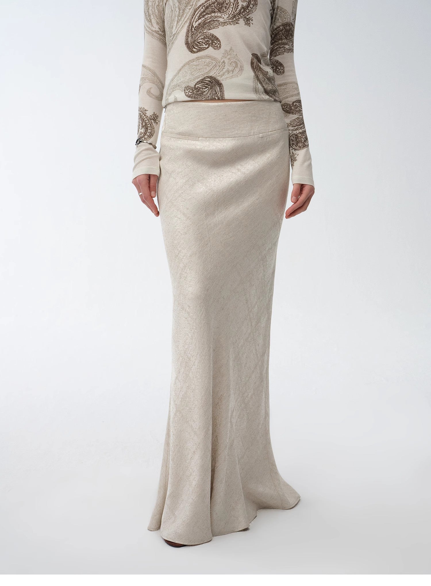 Person wearing a beige long skirt with a patterned top on a white background