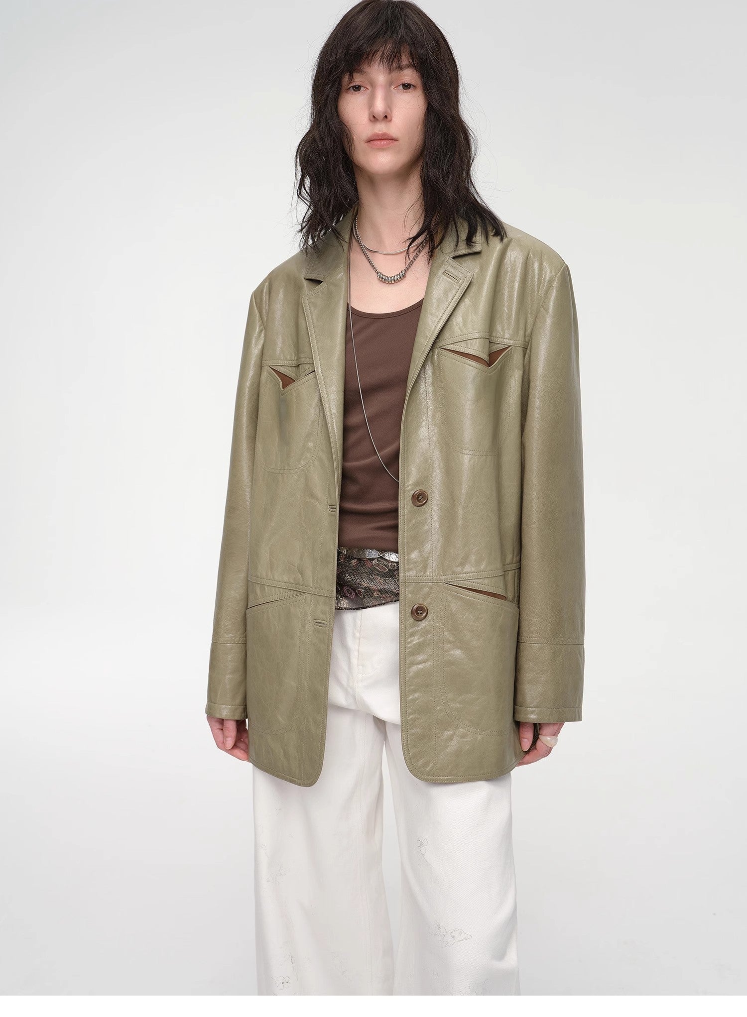 Person wearing a green jacket over a brown top and white pants on a white background