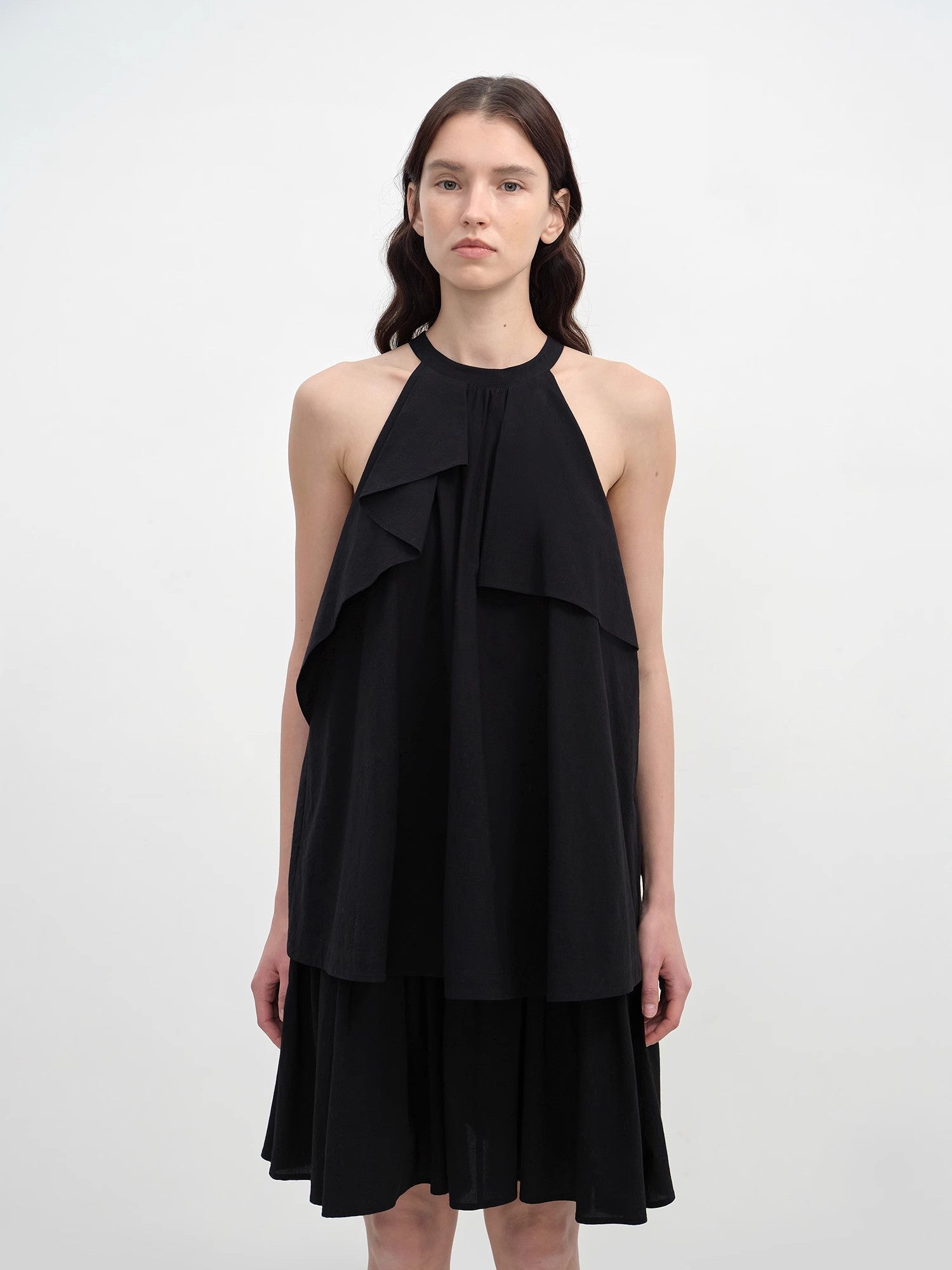 Woman wearing a black halter neck dress with layered design on a white background