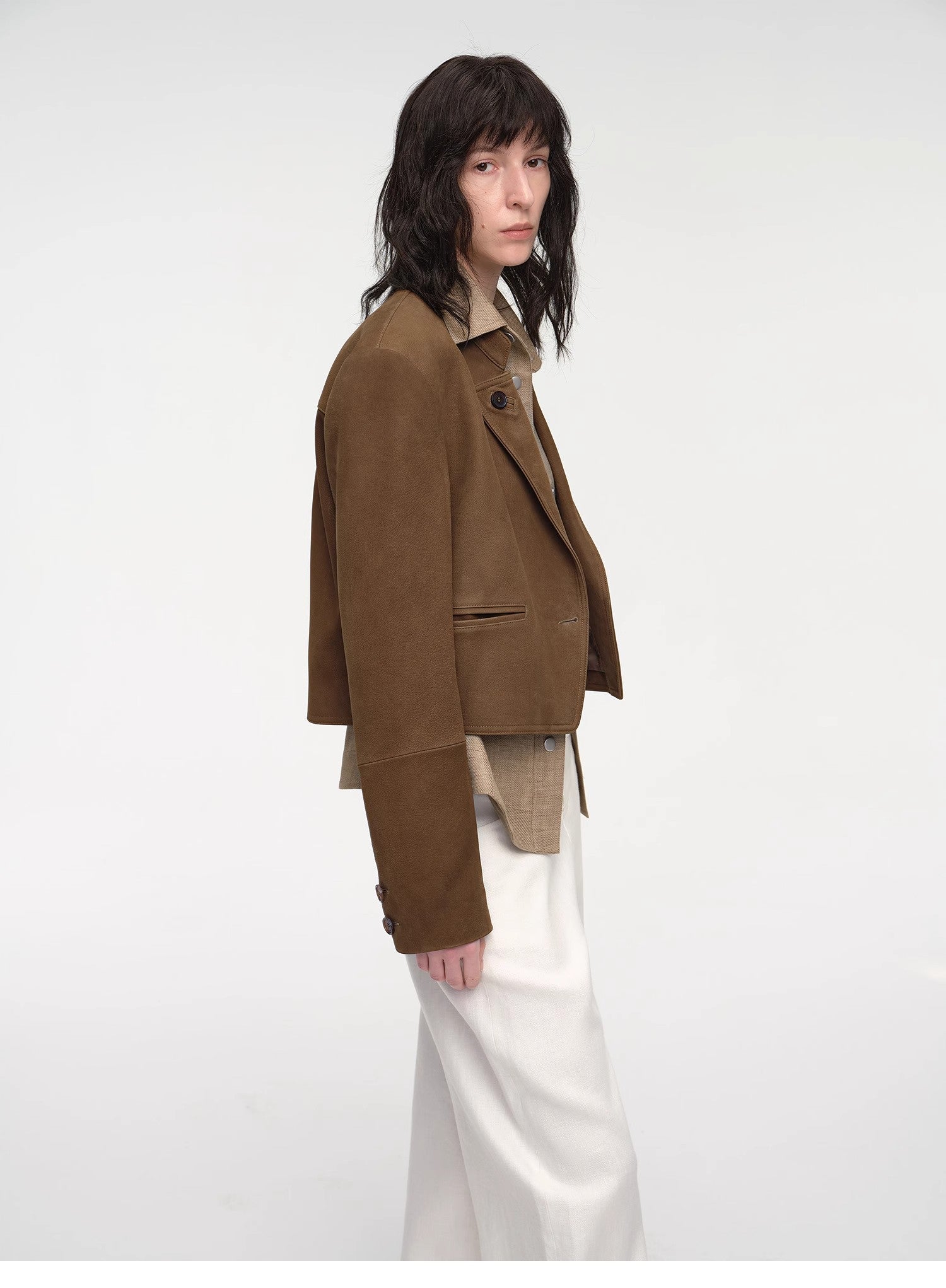 Person wearing a brown jacket over a beige shirt with white pants on a white background