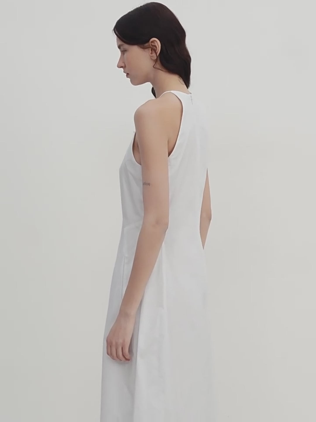 Woman wearing a light gray sleeveless dress against a white background
