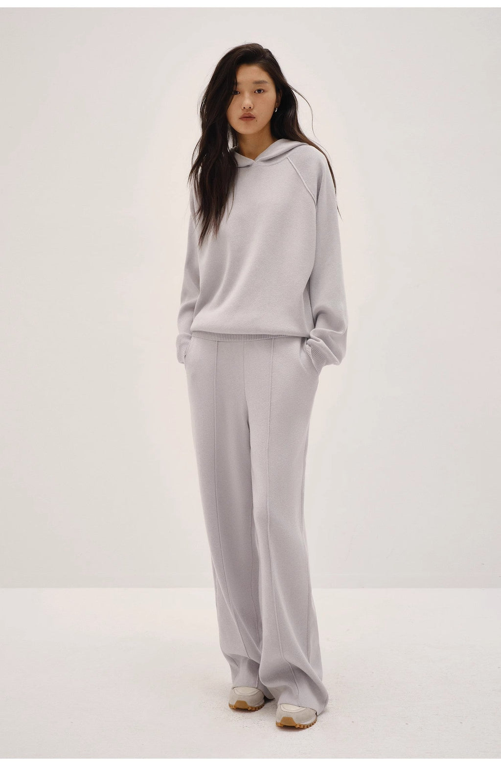 Person wearing a light gray hoodie and pants on a white background