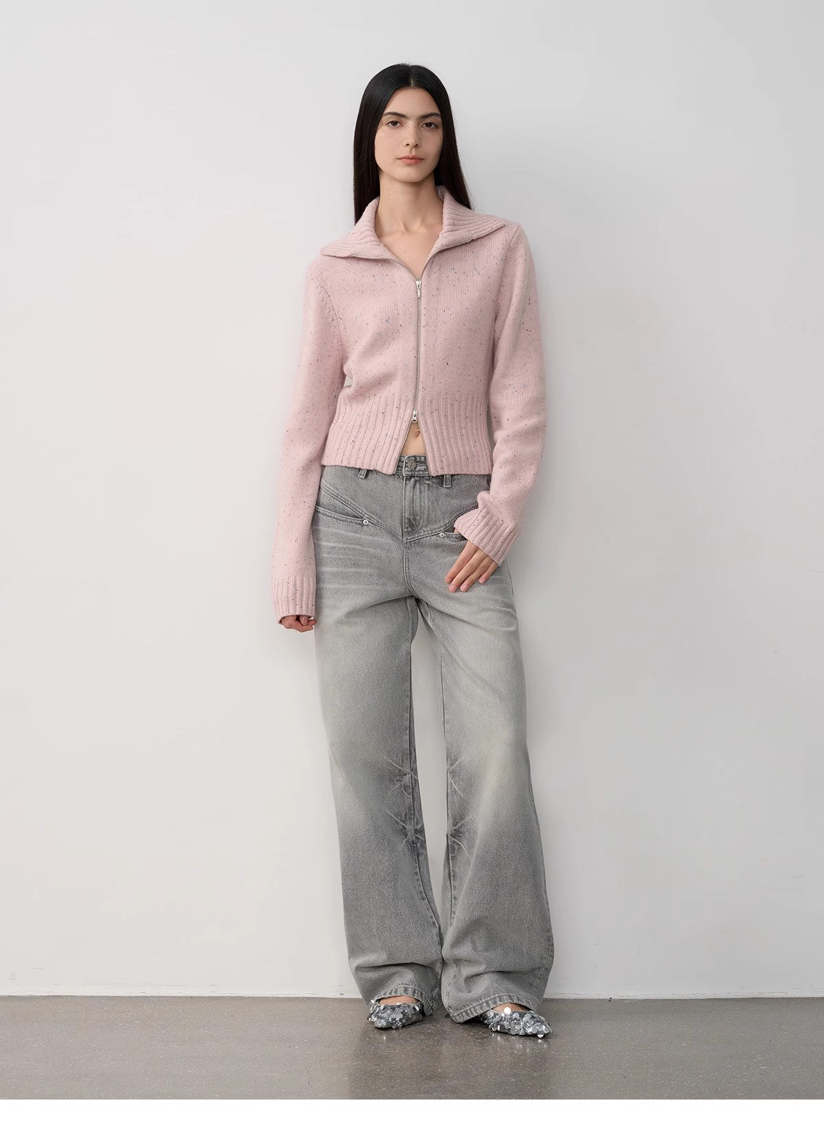 Woman wearing a pink sweater and gray pants against a white background