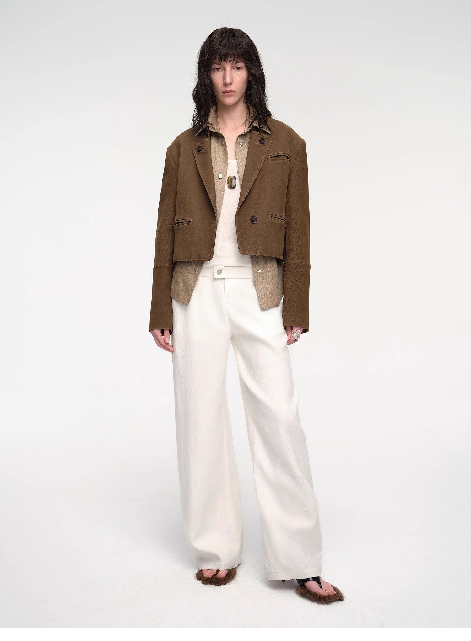 Person wearing a brown blazer and white pants on a white background