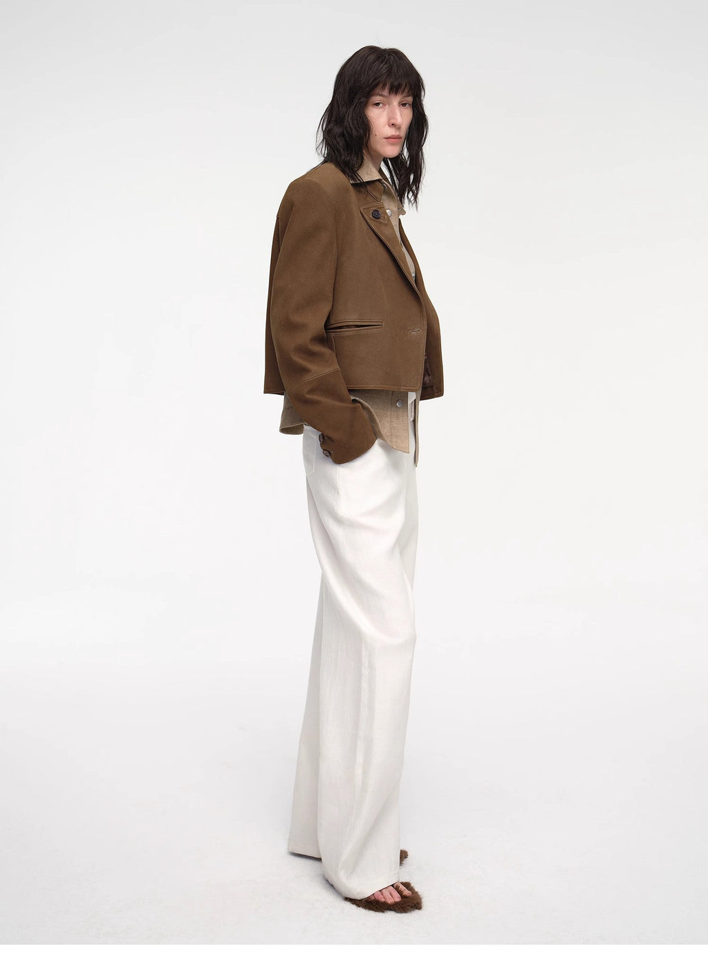 Person wearing a brown jacket and white pants on a white background