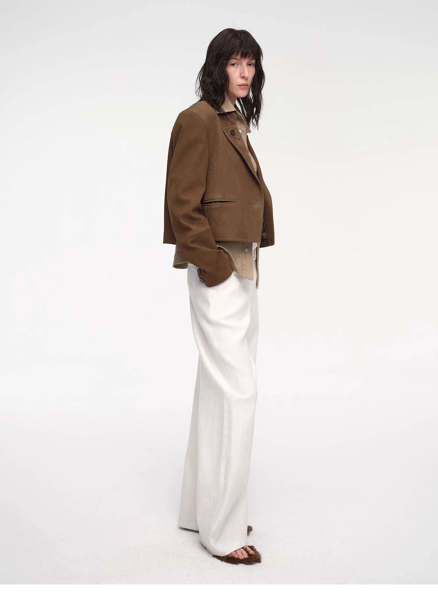 Person wearing a brown jacket and white pants on a white background