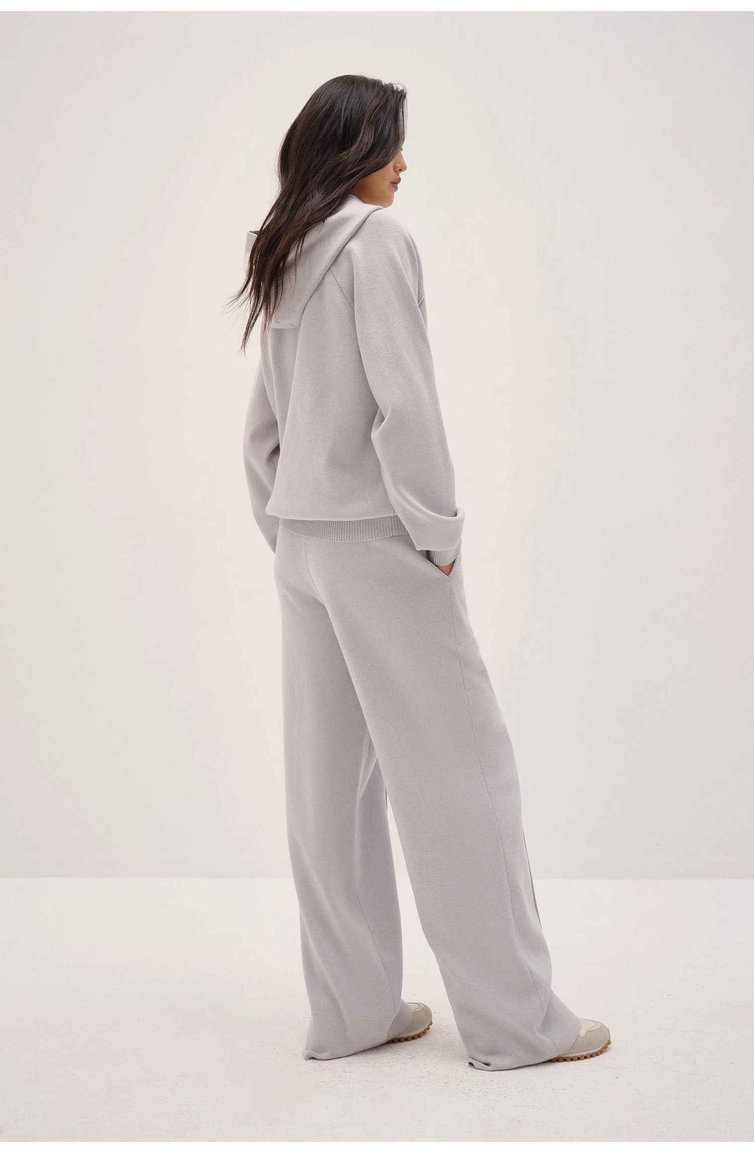 Person wearing a light gray hoodie and pants set on a white background