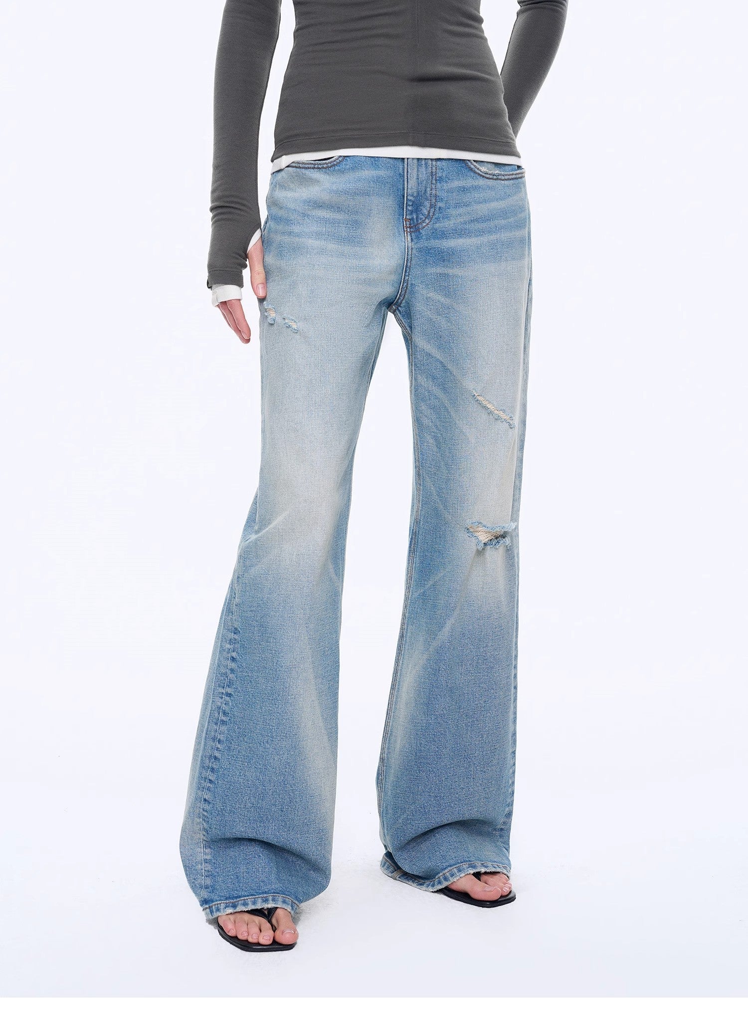 Person wearing blue flared jeans and a gray top on a white background