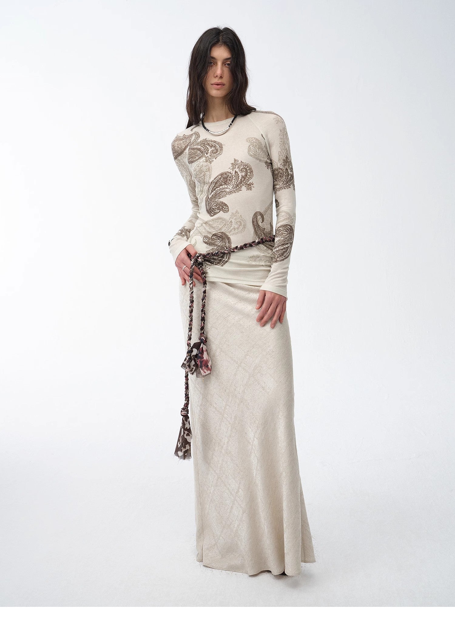 Woman wearing a long, light-colored dress with a patterned top on a white background