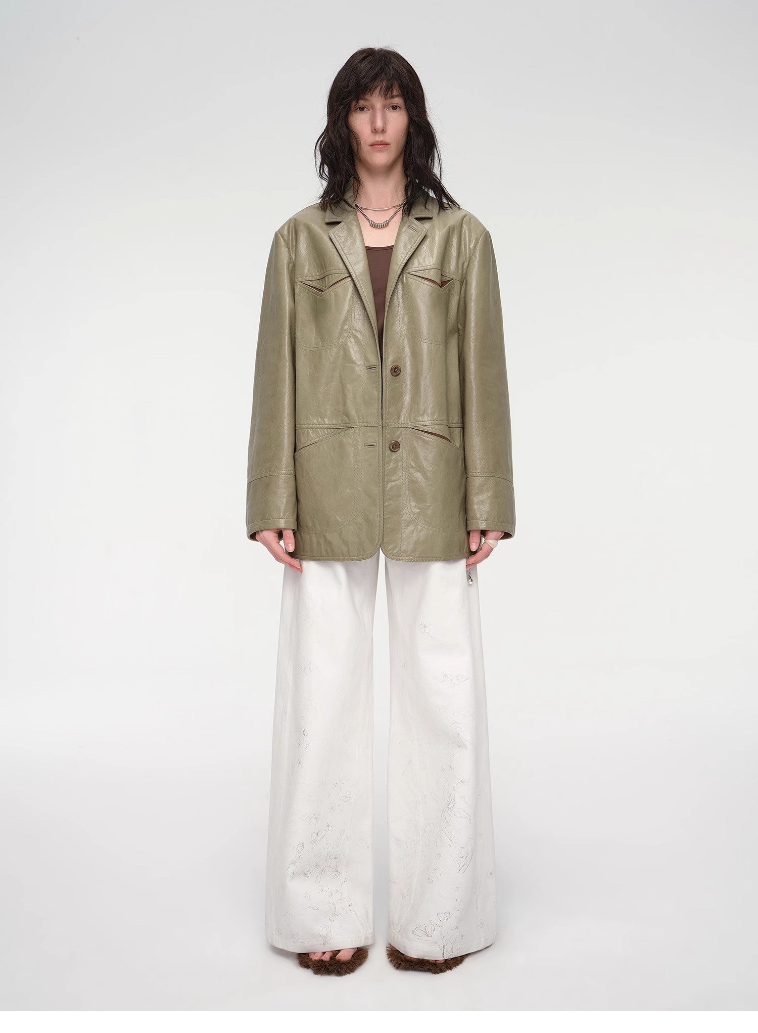 Person wearing a green leather jacket and white pants on a white background
