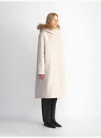 Woman wearing a long beige coat with fur hood on a white background