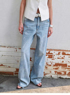 Person wearing light blue jeans standing against a textured wall.