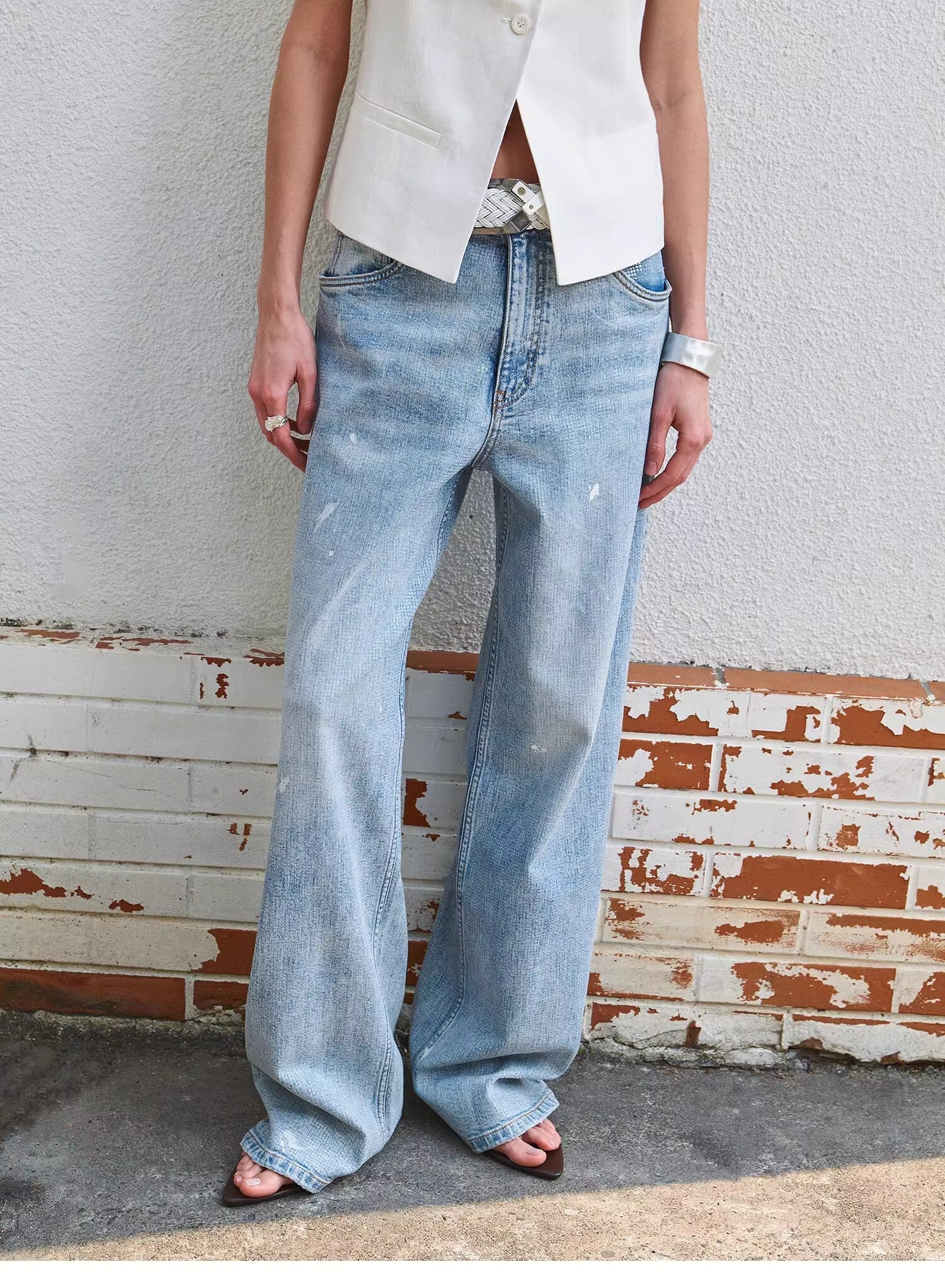 Person wearing light blue jeans standing against a textured wall.