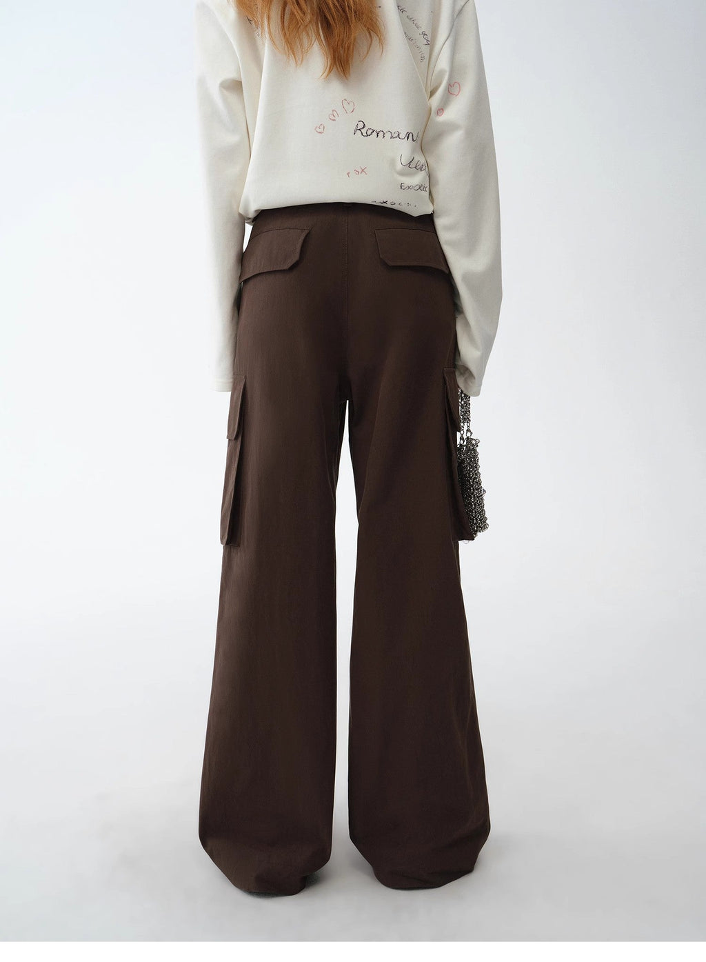 Person wearing a white sweatshirt with text and brown wide-leg pants on a white background