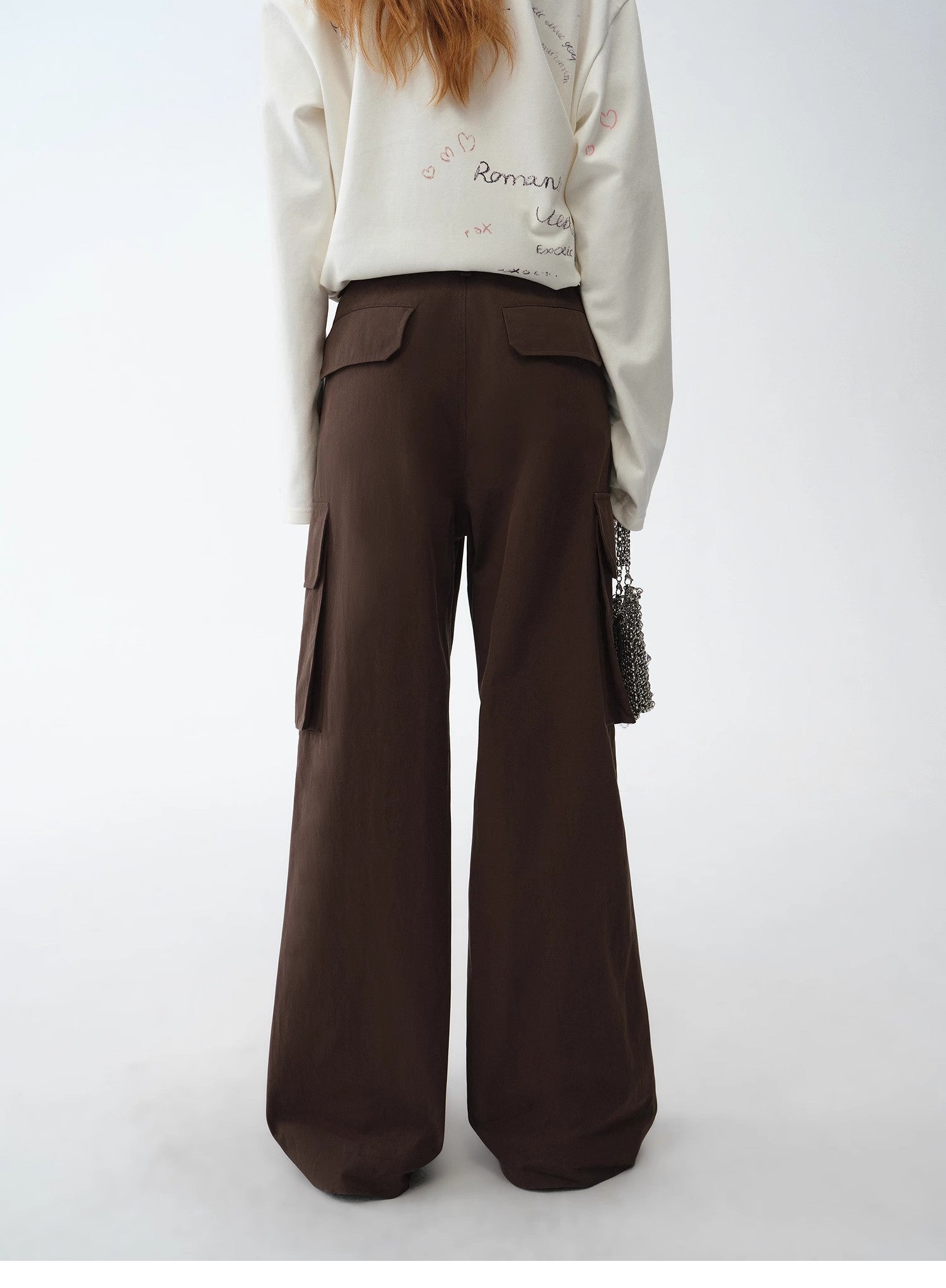 Person wearing a white sweatshirt with text and brown wide-leg pants on a white background
