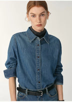 Woman wearing a blue denim shirt with a plain background