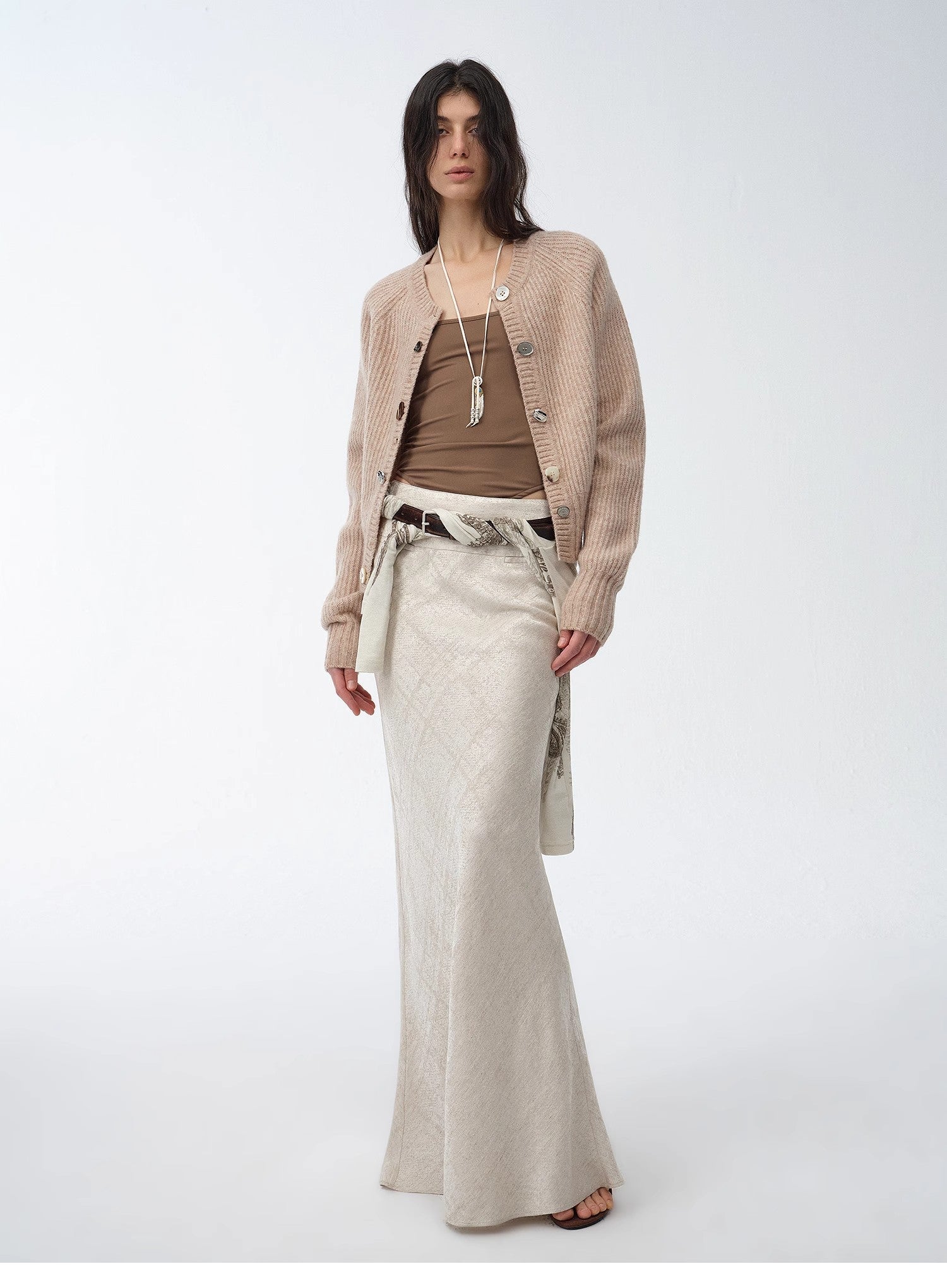Woman wearing a beige cardigan, brown top, and light-colored pants on a white background