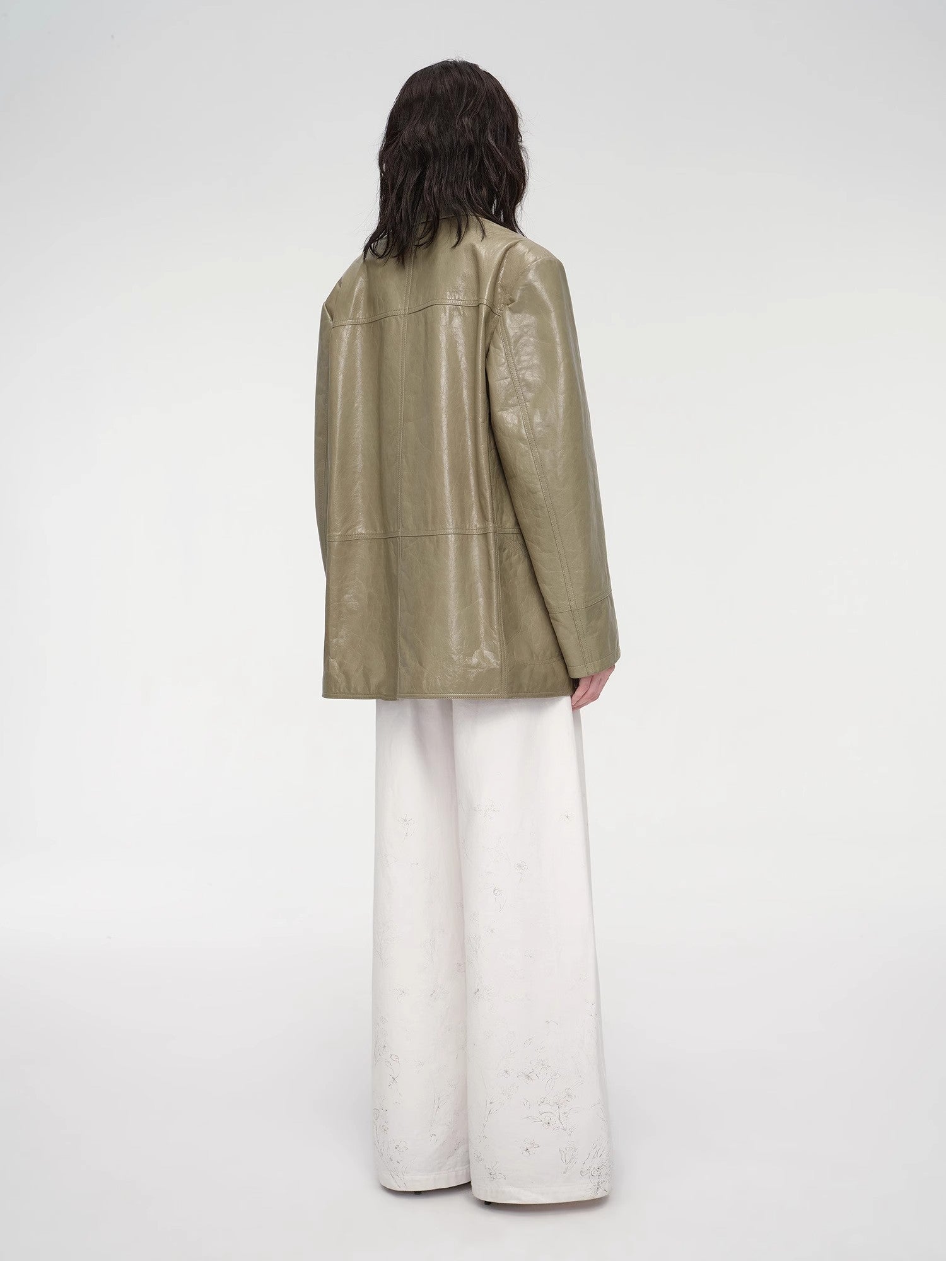 Person wearing a green leather jacket and white pants on a white background