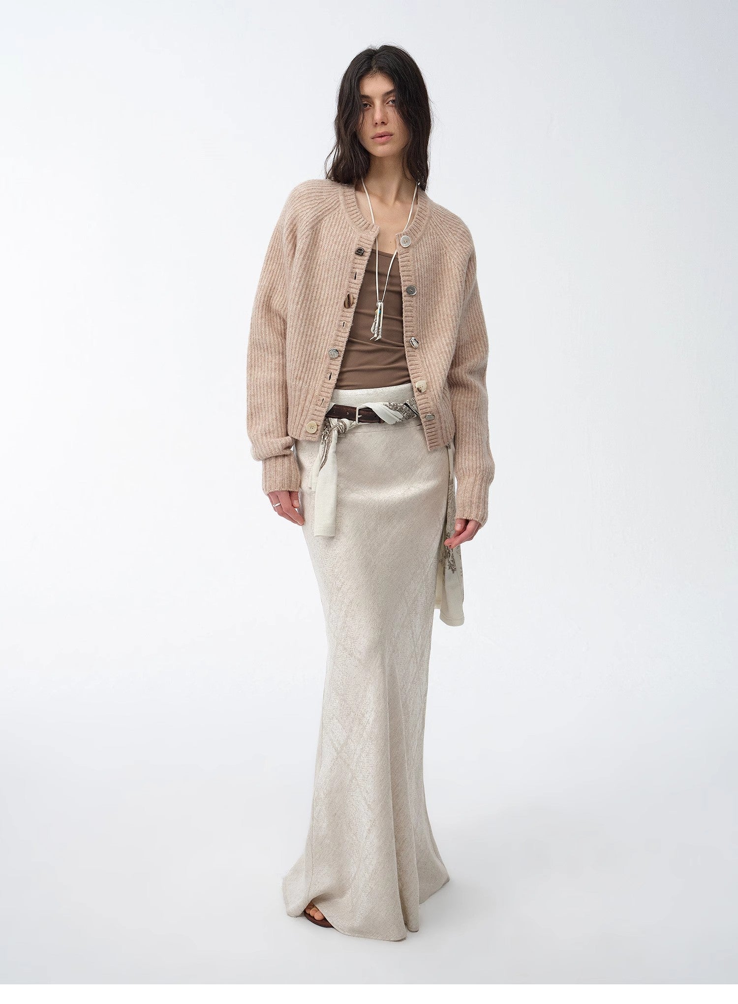 Woman wearing a beige cardigan, brown top, and beige pants on a white background