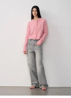Person wearing a pink cardigan and gray jeans against a white background