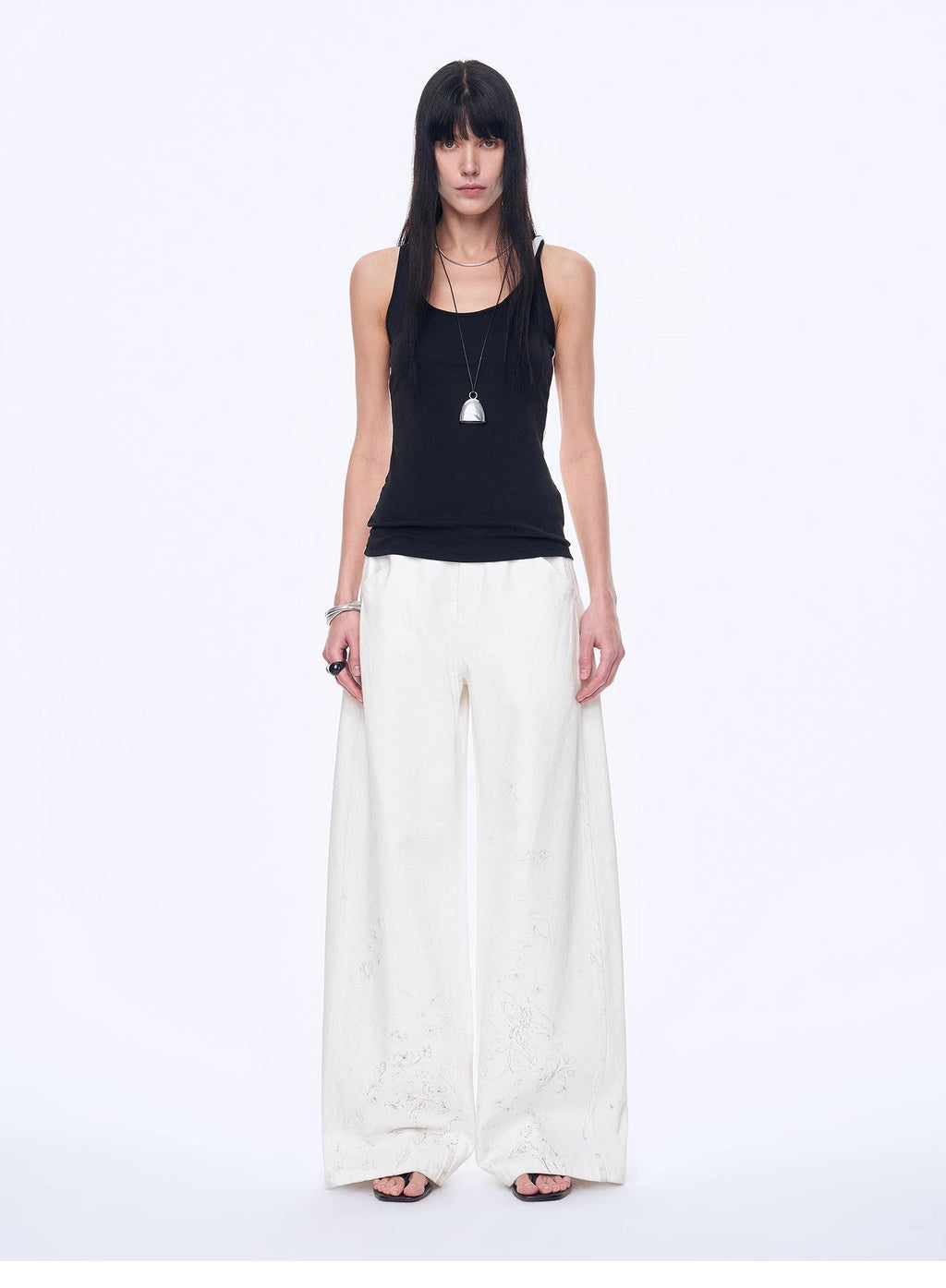 Woman wearing a black sleeveless top and white wide-leg pants on a white background
