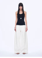 Woman wearing a black sleeveless top and white wide-leg pants on a white background