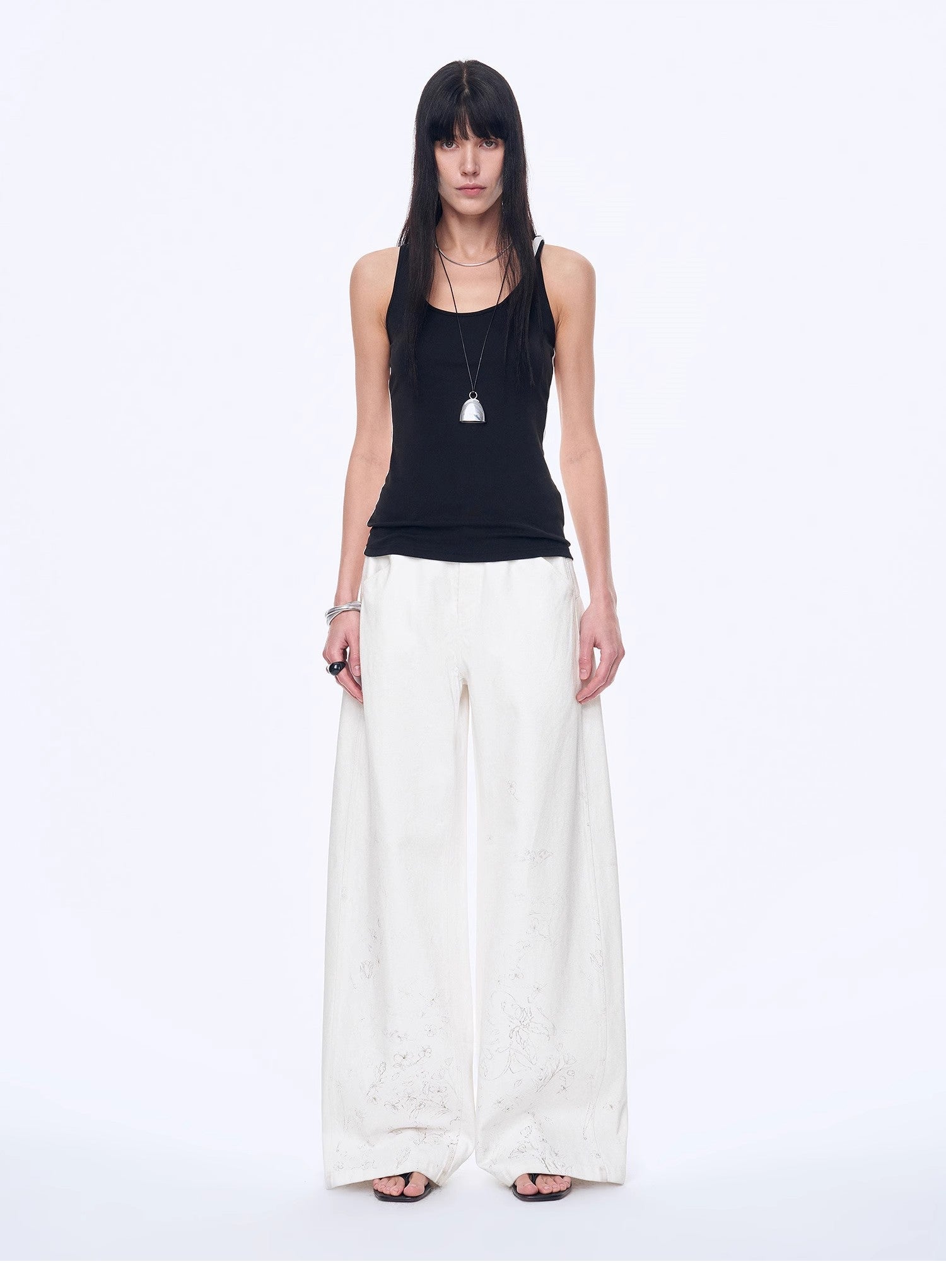 Woman wearing a black sleeveless top and white wide-leg pants on a white background