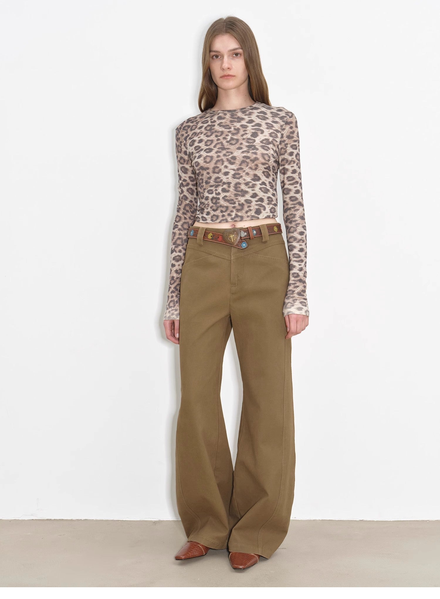 Woman wearing a leopard print top and brown pants on a white background
