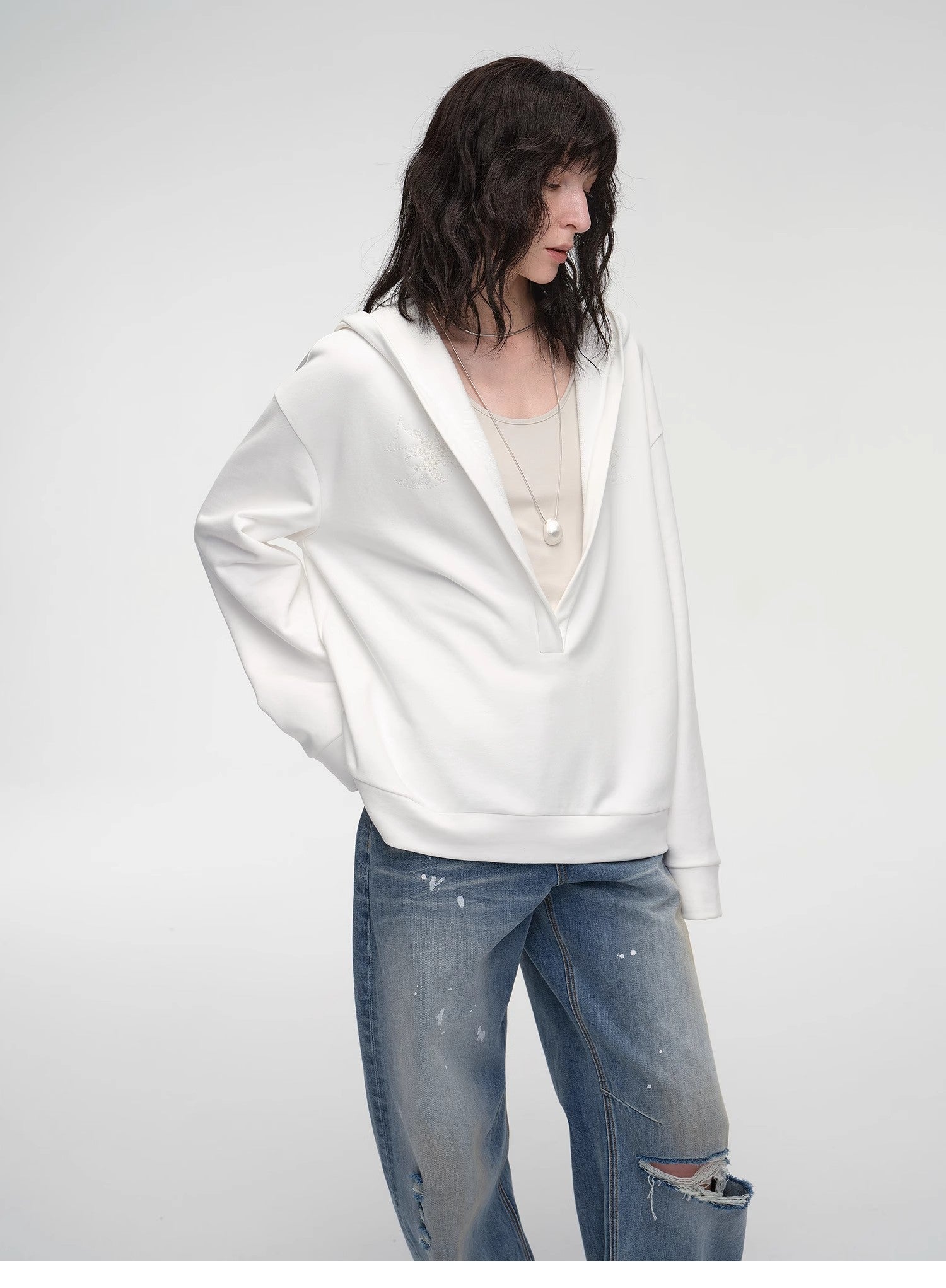 Person wearing a white oversized sweater and blue jeans on a plain background