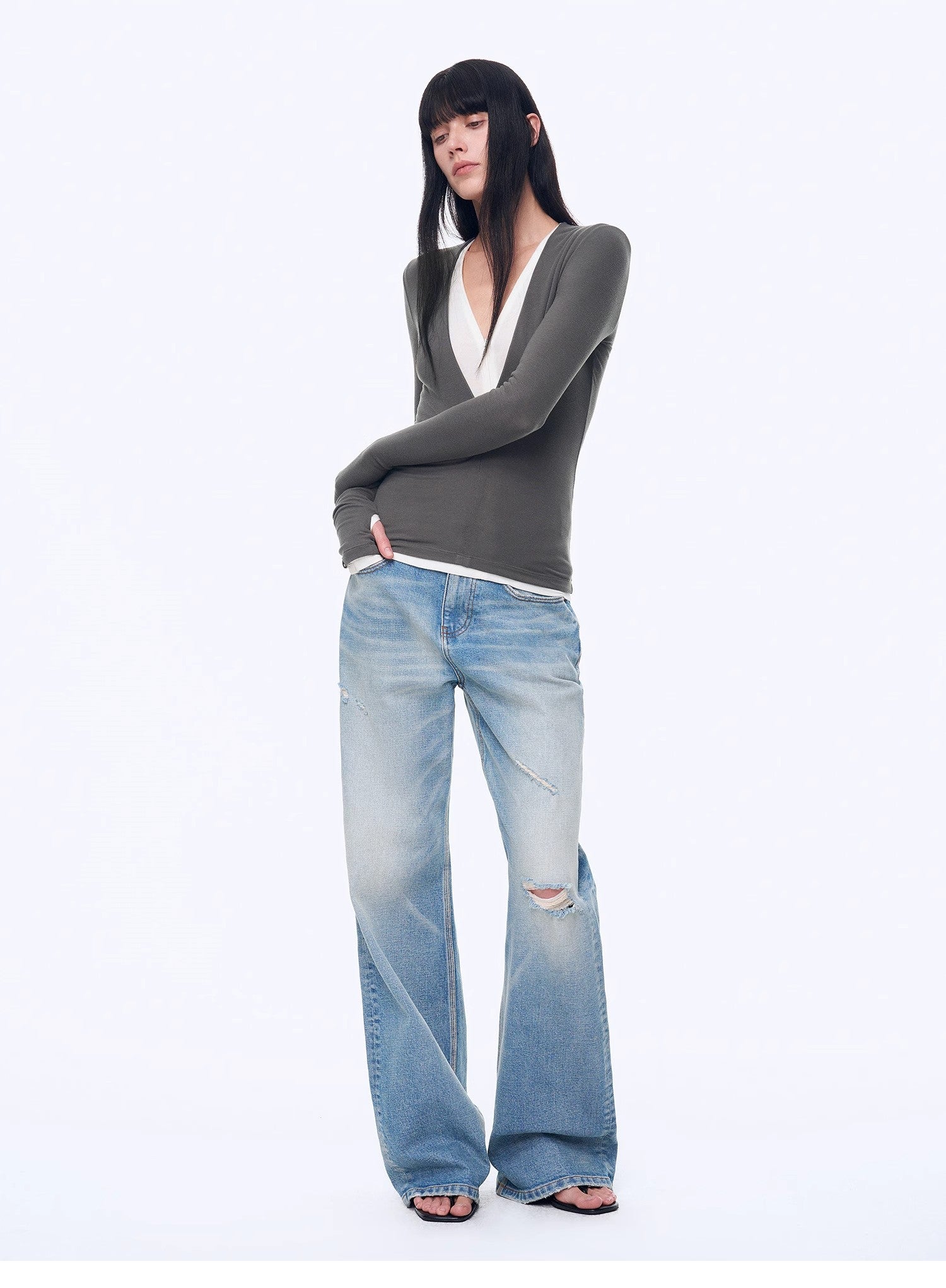 Person wearing a gray sweater and light blue jeans on a white background