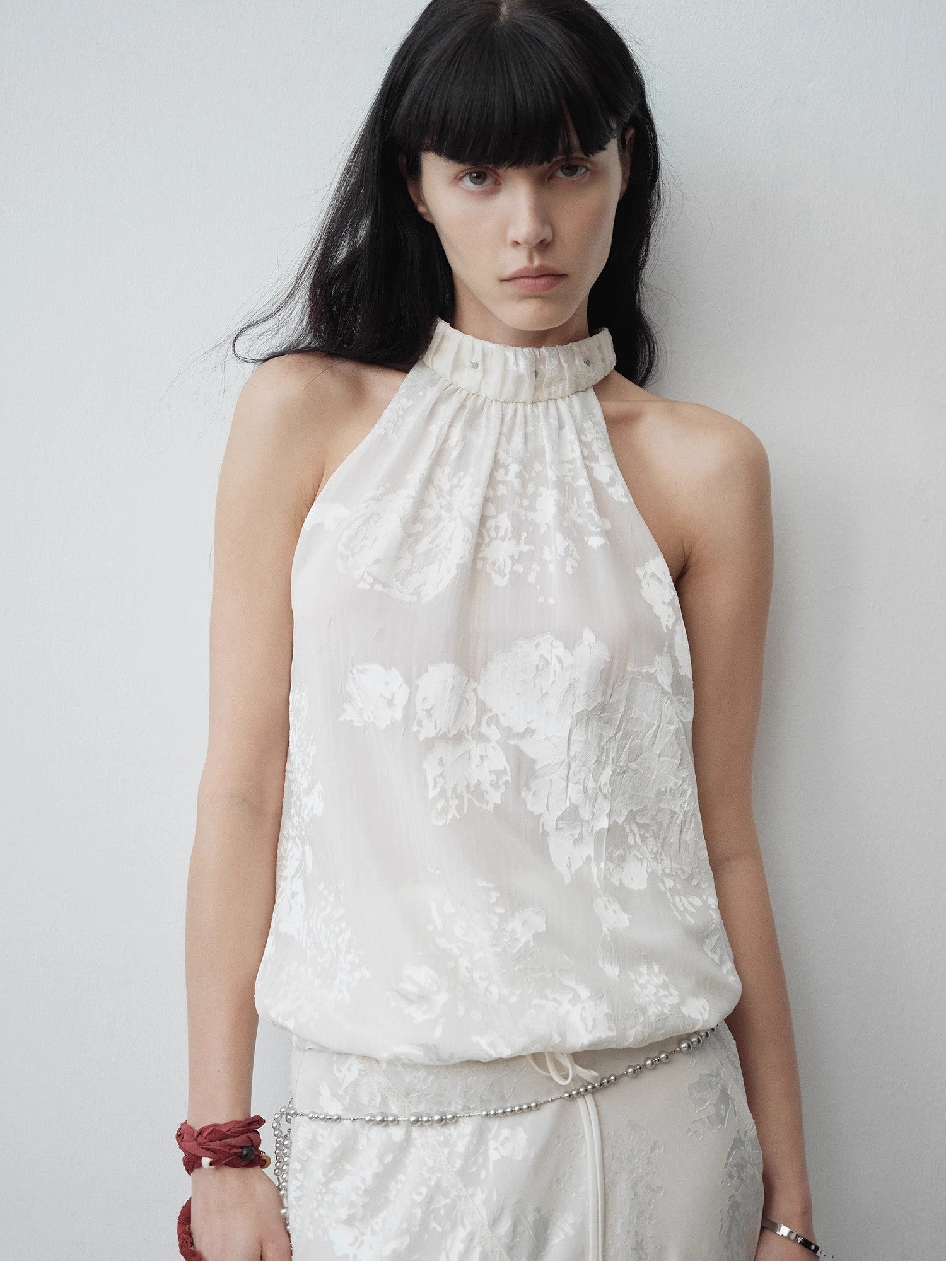 Woman wearing a white floral top against a plain background