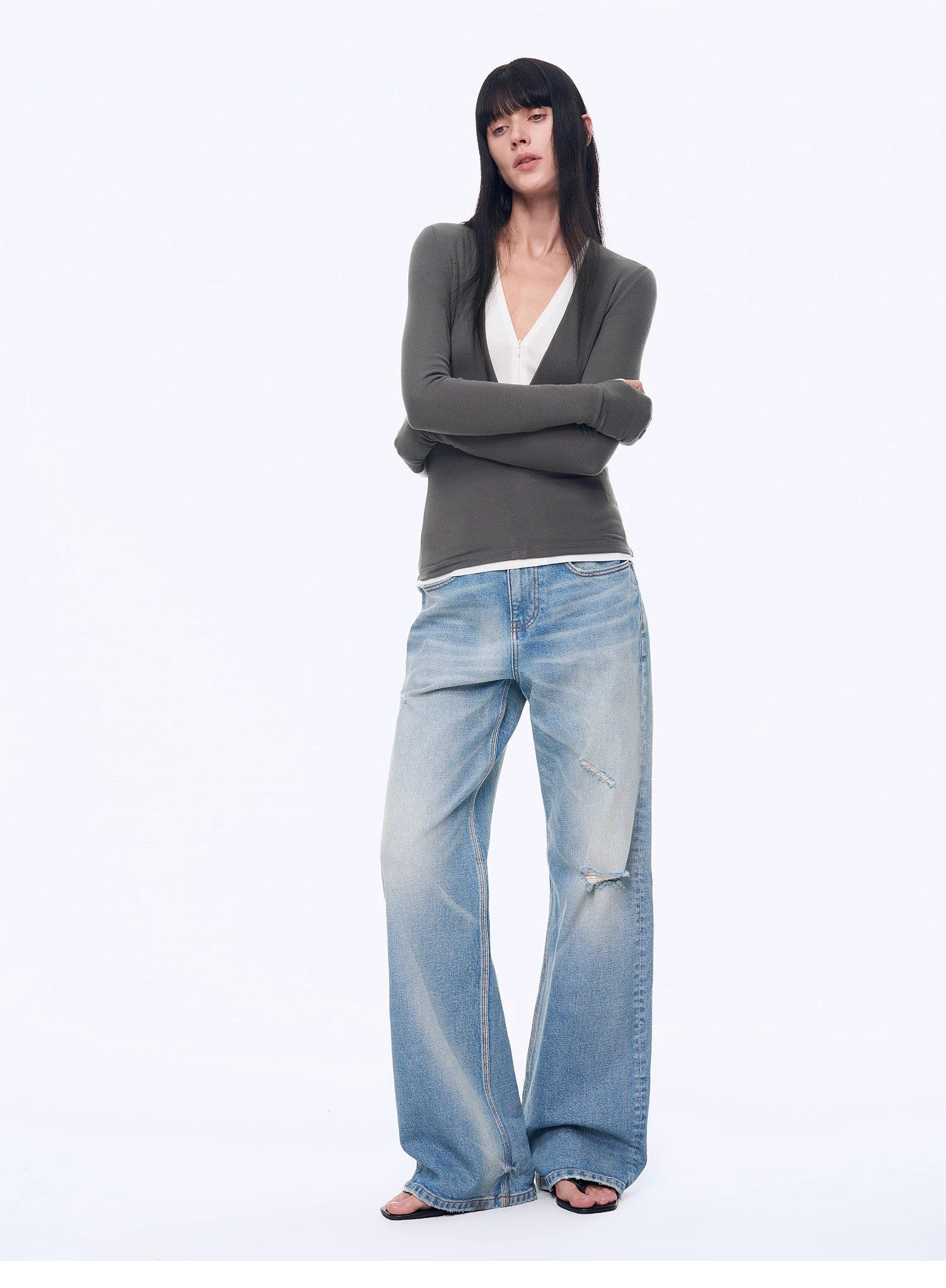 Woman wearing a gray sweater and blue jeans on a white background