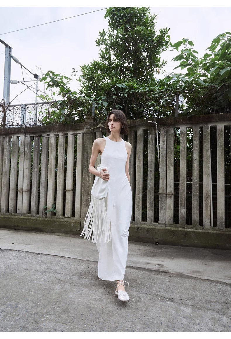 Woman in a white dress with fringe holding a white bag, standing in front of a wooden fence.