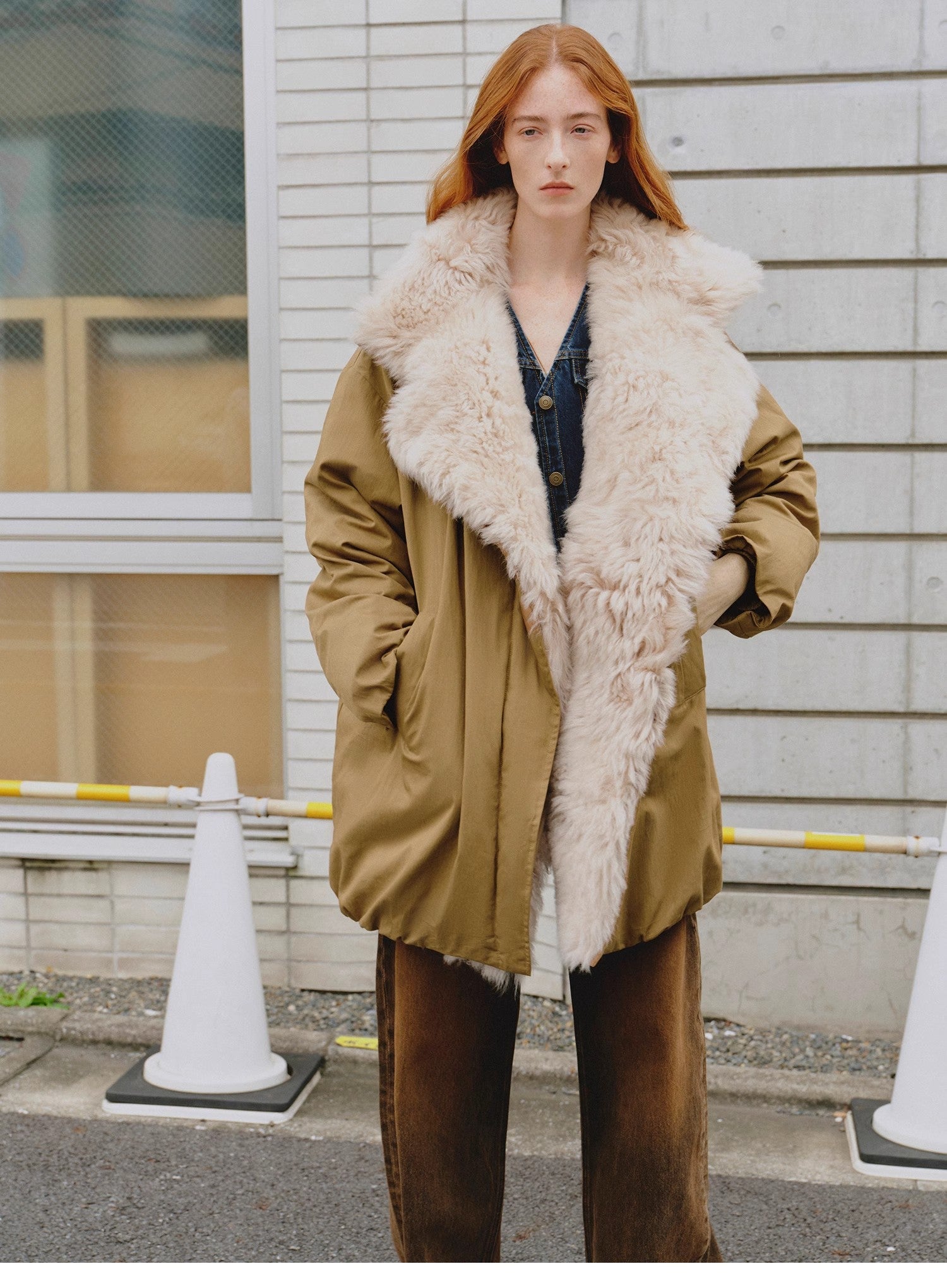 Person wearing a brown coat with a fur-lined hood standing outdoors.