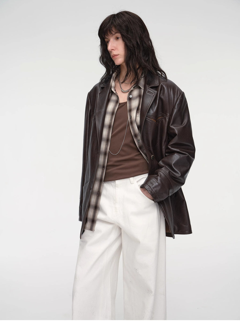 Person wearing a brown leather jacket over a plaid shirt with a white background