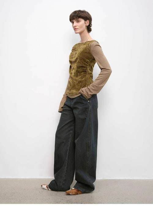 Woman wearing a green top and dark pants against a white wall
