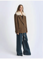 Person wearing a brown coat with fur collar and blue jeans on a white background