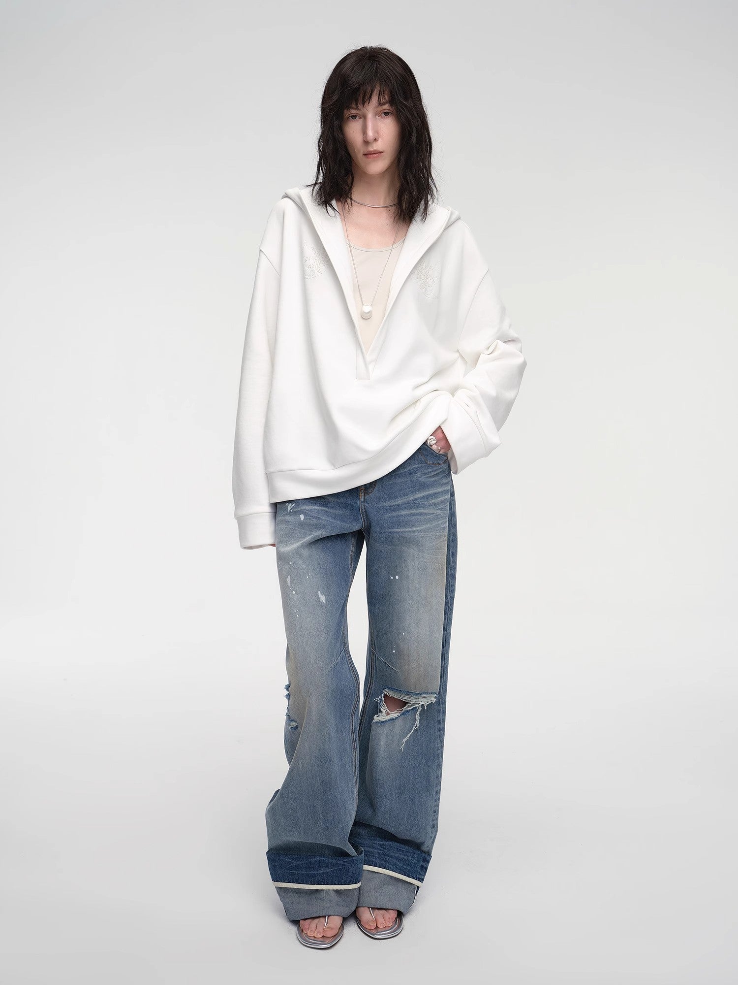 Person wearing a white oversized hoodie and blue distressed jeans on a plain background